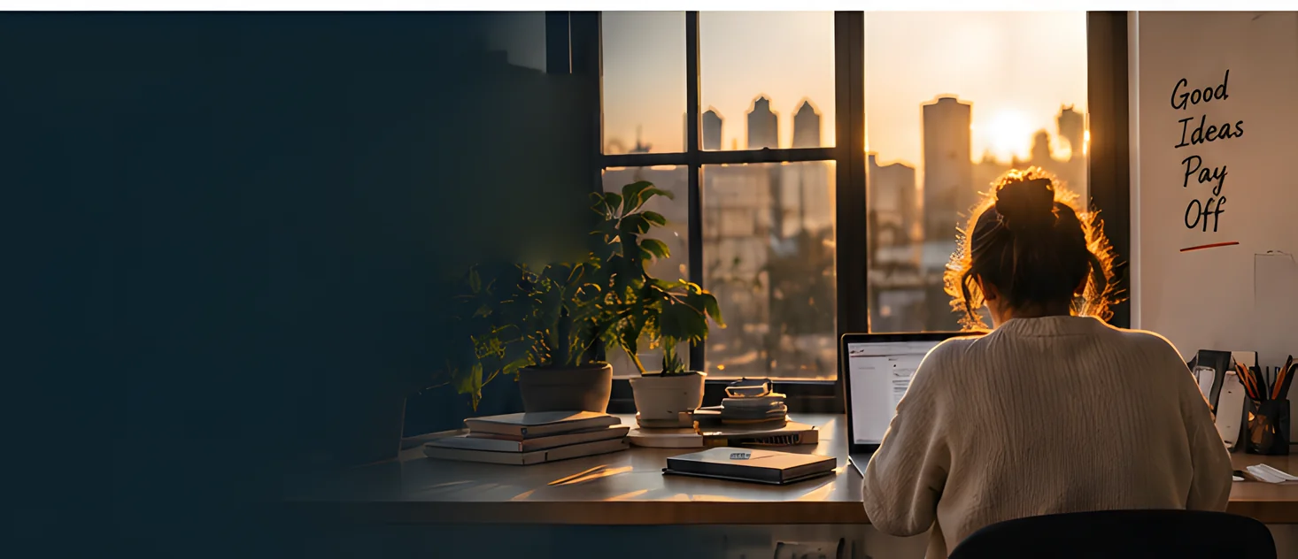 A freelancer working at a laptop by a window at sunset, a handwritten note on the wall reading Good Ideas Pay Off